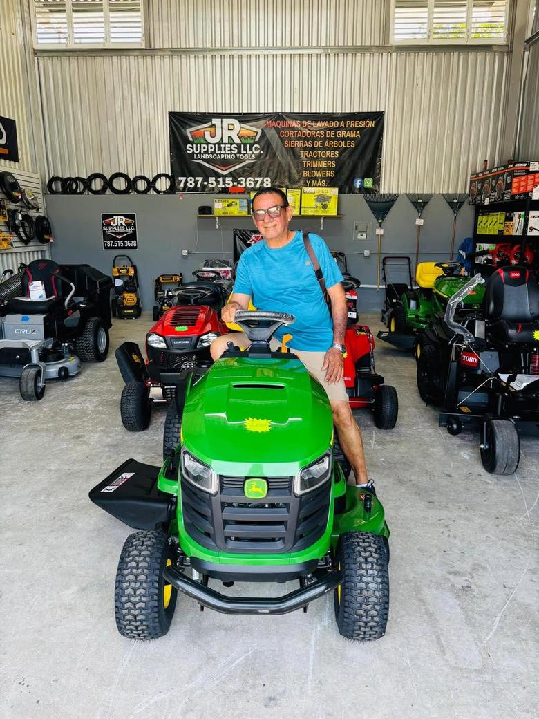 Cliente de JR Supplies sentado en un tractor de jardín John Deere verde